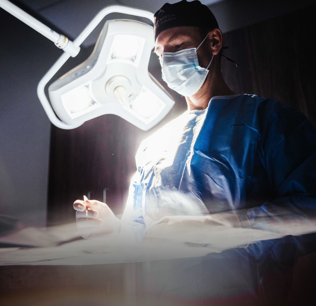 Surgeon in scrubs under bright surgical lights.