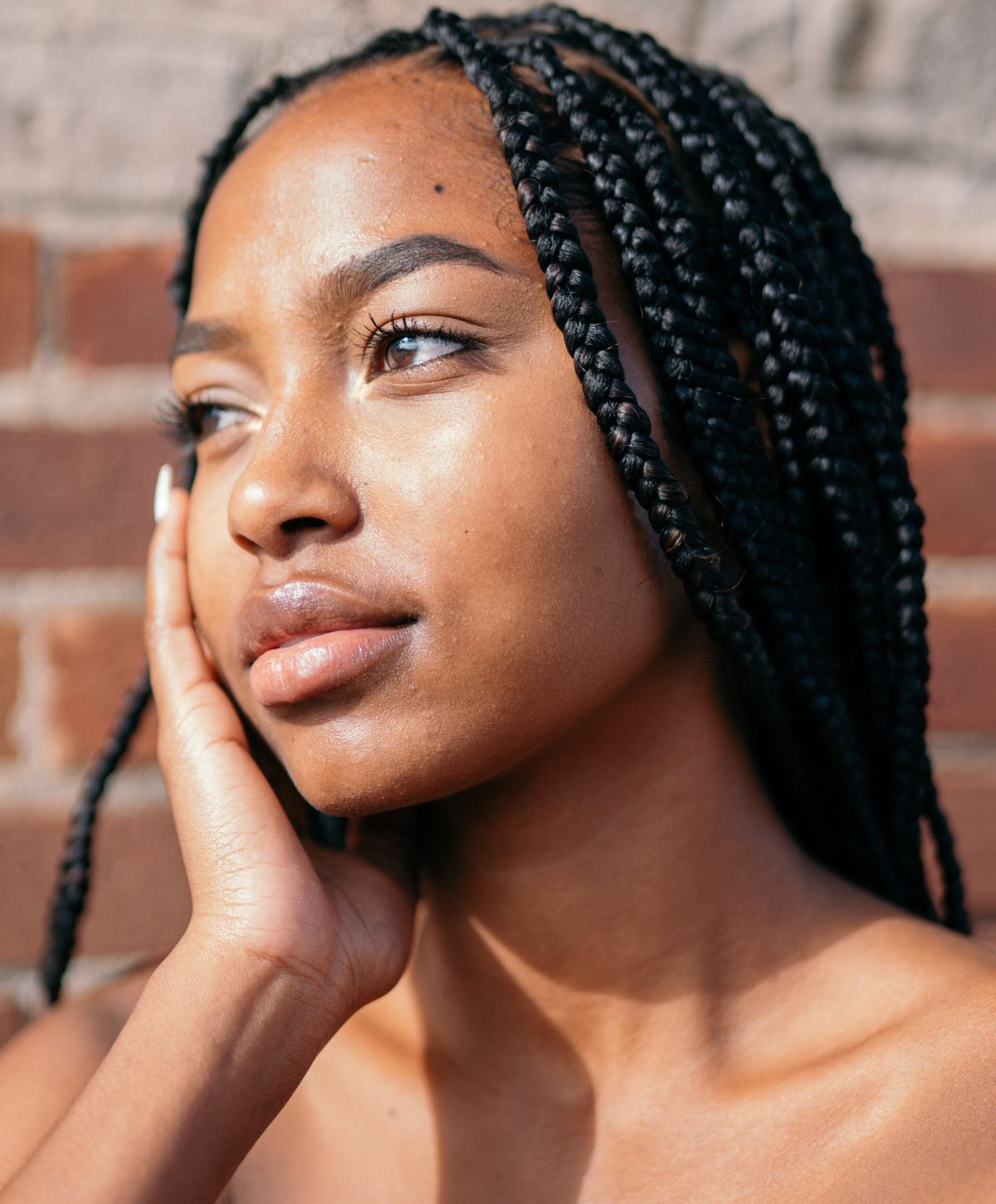 Young woman with braids, thoughtful expression against brick.