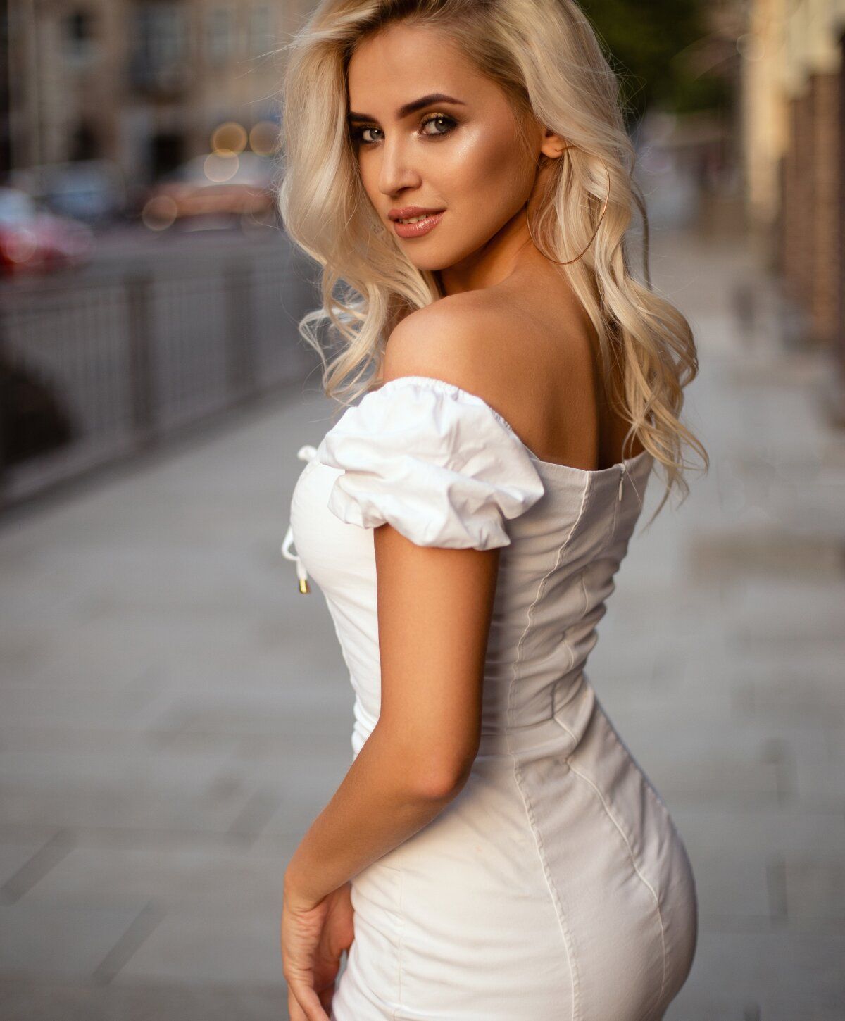 Blonde woman in elegant white dress outdoors.