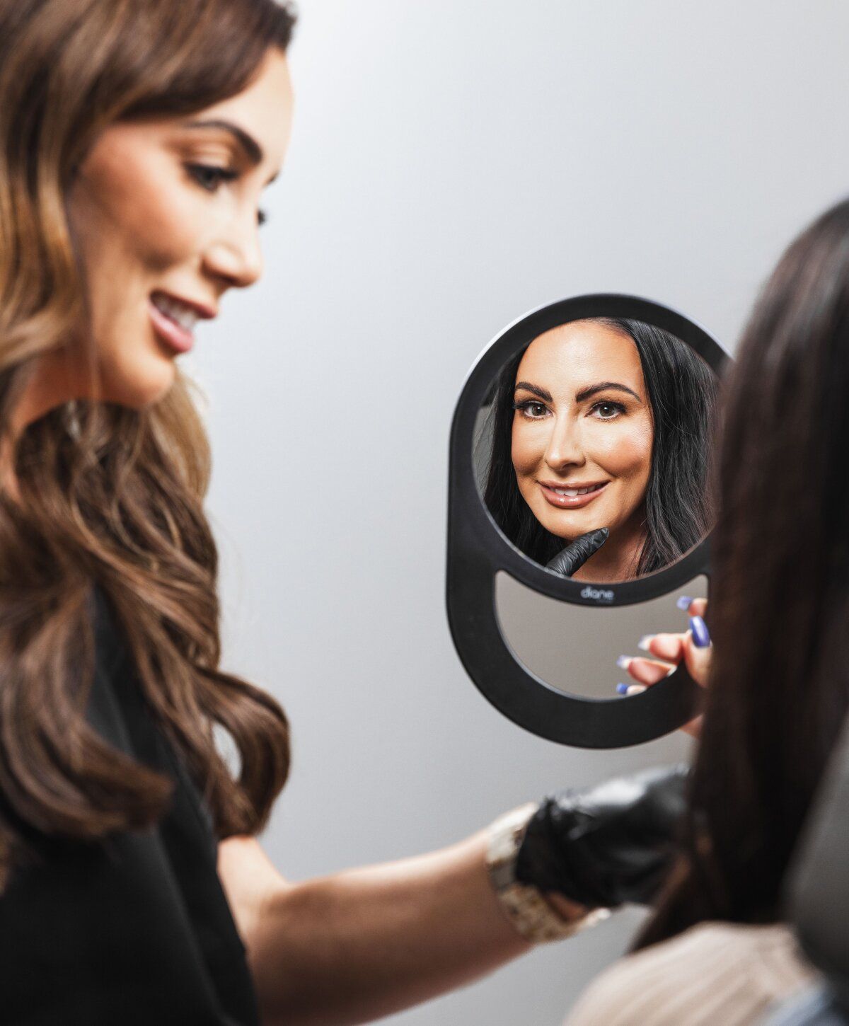 Stylist assisting client with hair in mirror.