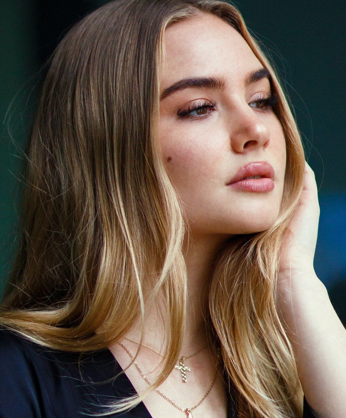 Woman with long hair contemplatively touching her face.