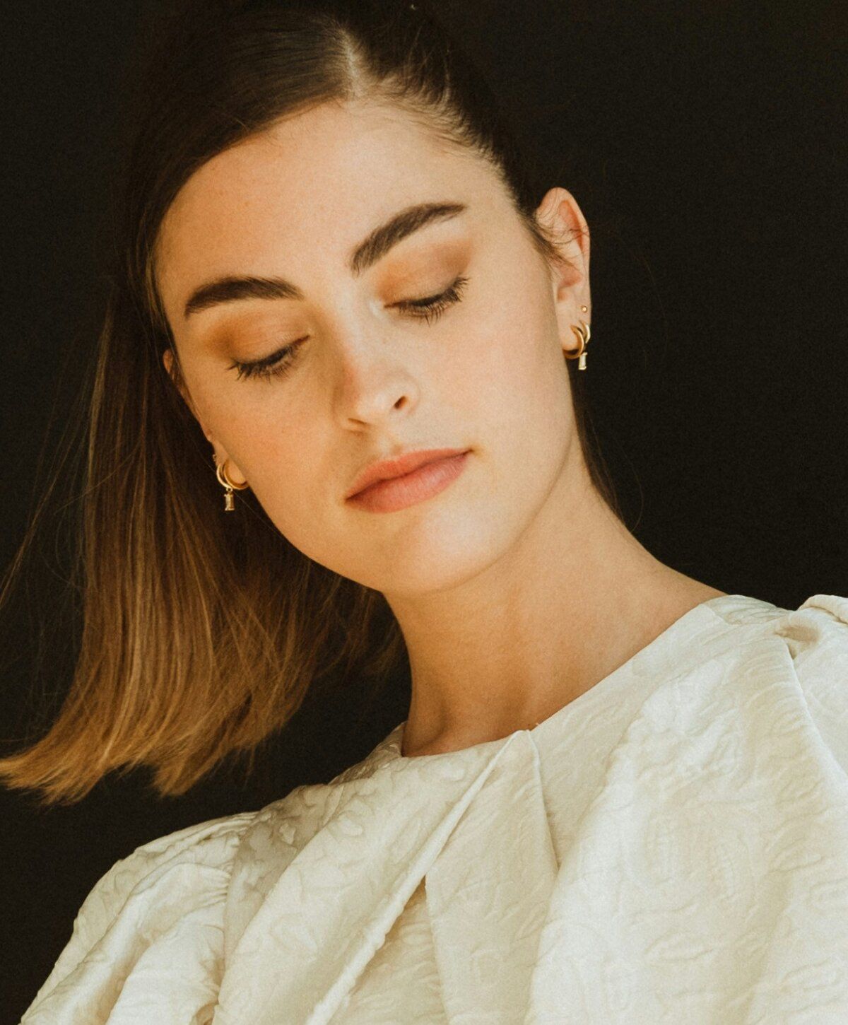 Woman in white dress with earrings looking down.