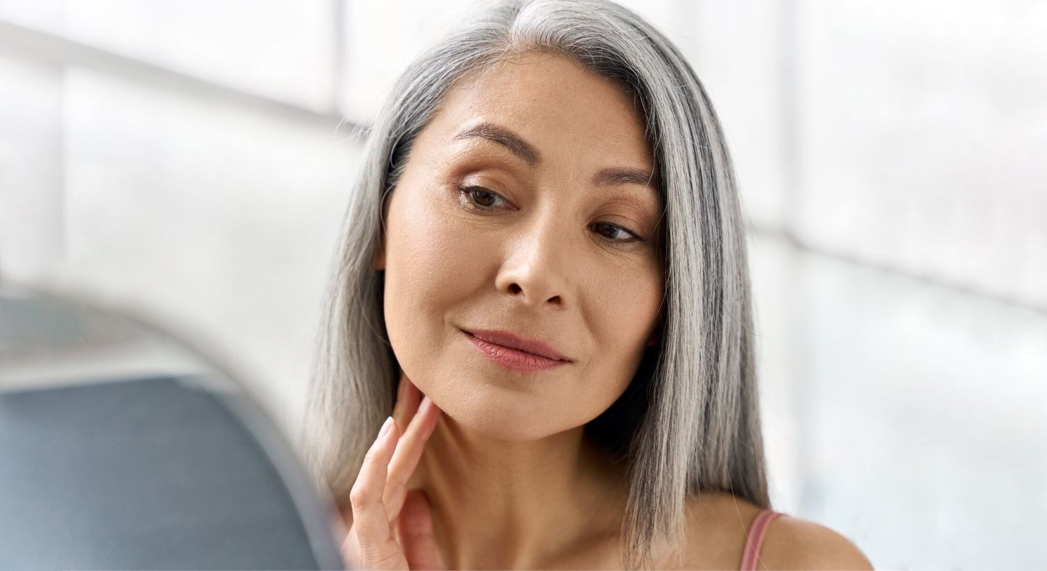 Woman examining her skin in mirror reflection.