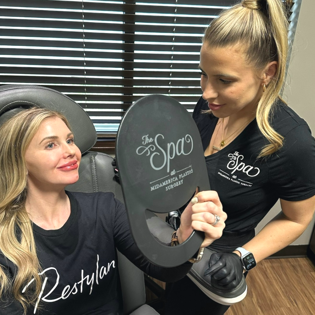 blonde patient at The Spa at MidAmerica Plastic Surgery in Glen Carbon, IL, admiring the results of her lip filler in mirror.